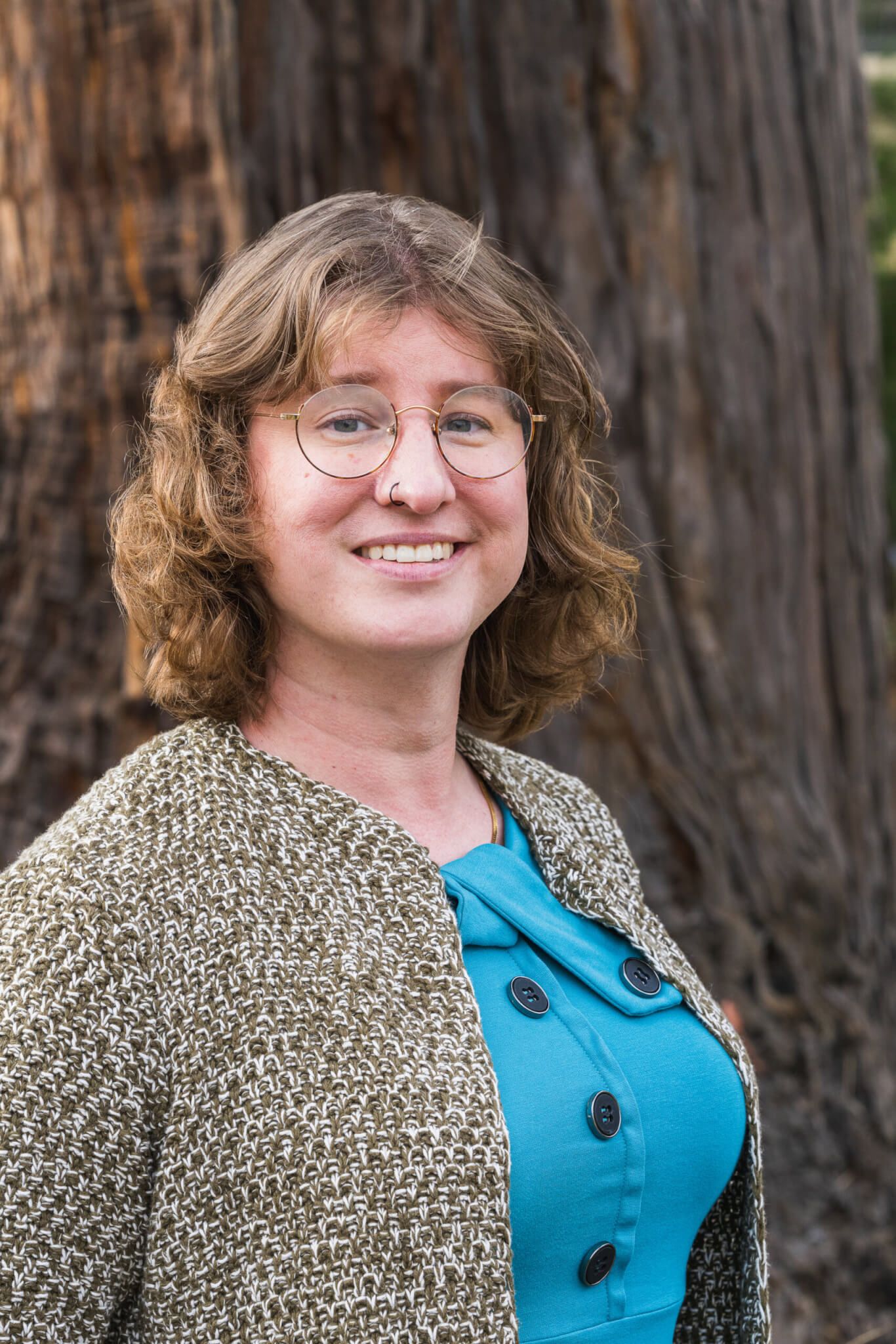 Rory Morris smiles into the camera in front of a mature redwood tree, by Orenda Randuch