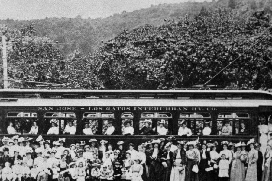 Black-and-white photo of a crowded San Jose–Los Gatos Interurban Railway car with many people, some seated inside and many standing in front, posing for the camera; trees and hills in the background.