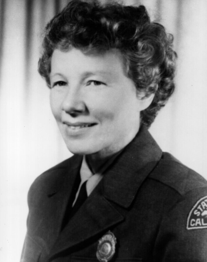 Black-and-white portrait of a person in uniform with short curly hair, smiling slightly.